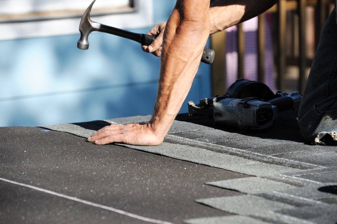 An image of a person with a hammer working on a roof repair service